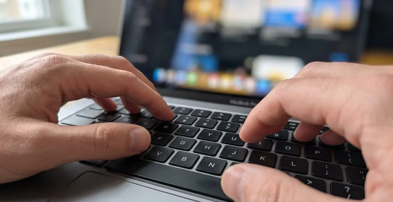 Primo piano di mani che digitano su una tastiera di laptop moderno con schermo completamente sfocato sullo sfondo